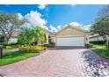 Charming tan single-story home featuring mature landscaping, a brick paver driveway, and a two-car garage at 2900 Grasslands Dr, Lakeland, FL 33803
