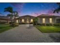Elegant home featuring stucco facade, arched windows, double door entry, manicured landscaping, and brick paver driveway at dusk at 565 Osprey Landing Dr, Lakeland, FL 33813