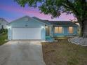 Charming light blue single-story home with a well-maintained lawn and two-car garage at dusk at 1064 Penguin Pl, Lakeland, FL 33809