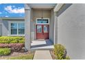 Close-up of a red double-door entryway with sidelights, set in a gray home with manicured landscaping at 6185 Gracie Pl, Lakeland, FL 33812