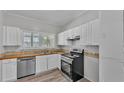 Bright kitchen featuring white cabinets, stainless steel appliances, and wood-look vinyl flooring at 2203 Avenue F Nw, Winter Haven, FL 33880