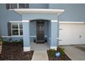 Covered front entrance with gray door, trimmed pillars, and manicured landscaping at a lovely two-story home at 3882 Resting Robin Ave, Bartow, FL 33830