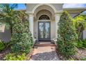 Elegant front entrance with double doors, decorative columns, and a brick walkway surrounded by lush greenery at 2743 Verandah Vue Way, Lakeland, FL 33812