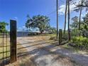 Gated driveway leads to a single-story home featuring a metal roof, large shade tree, and attached two-car garage at 2171 Sophia S Pl, Lakeland, FL 33811