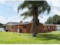 Back exterior of the home featuring a well-maintained lawn, palm trees, brick accents, and a covered porch at 1208 W Lake Buckeye Dr, Winter Haven, FL 33881