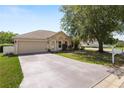 View of a one-story home with beige siding, a well-manicured lawn, and a two-car garage at 5733 Oakwood Knoll Dr, Lakeland, FL 33811