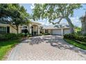 Stunning exterior view of the home with a three-car garage, mature trees, and a brick-paved driveway at 645 Whisper Woods Dr, Lakeland, FL 33813