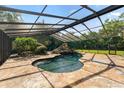A screened in pool features a unique rock feature and is surrounded by stone flooring at 5425 Lewellyn Rd, Lakeland, FL 33810