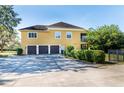 Rear view of a three-story yellow home featuring a three-car garage and manicured hedges at 3020 Crews Lake Dr, Lakeland, FL 33813