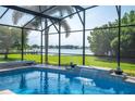 Relaxing pool with a waterfall feature, screened enclosure, and scenic views of the water at 7016 Summit Cir, Winter Haven, FL 33884