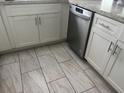 Close-up of the kitchen featuring tiled floors, white cabinetry, gray counters, and stainless steel dishwasher at 3646 Sherertz Road, Lakeland, FL 33810