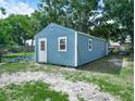 A bright blue shed with white trim sits on a grassy lot with trees in the background at 2120 Dille St, Lakeland, FL 33815