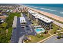 Aerial view showcasing the condo, parking, and inviting pool with lounge chairs next to the beautiful ocean at 3180 Ocean Shore Blvd # 208, Ormond Beach, FL 32176