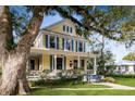 Two-story yellow house with a wraparound porch and large shade tree at 608 Magnolia St, New Smyrna Beach, FL 32168