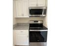This kitchen features stainless steel appliances, including a microwave and range, with white cabinets and granite countertops at 128 Orange Ave, Edgewater, FL 32132