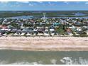 Aerial view of a coastal neighborhood, with homes lined along a sandy beach against a blue sky with white clouds at 6443 Engram Rd, New Smyrna Beach, FL 32169