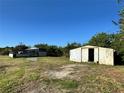 Exterior view of weathered outbuildings, surrounded by an unkempt grassy yard and clear blue sky at 3890 Skyway Dr, Sanford, FL 32773