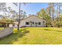 Rear view of home surrounded by mature trees, featuring a large backyard, and covered patio area at 1910 Botree Ct, Port Orange, FL 32128
