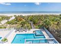 Aerial view of a pool and hot tub with beach access beyond lush greenery and ocean views at 1373 N Atlantic Ave, New Smyrna Beach, FL 32169