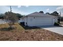 Side view of the home featuring a white brick facade, well-manicured lawn, and an attached two-car garage at 1077 Willow Wood Dr, Port Orange, FL 32129