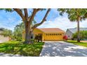 Charming yellow single-story home featuring a well-manicured lawn, a large tree, and an attached two-car garage at 706 Sky Tree Ct, New Smyrna Beach, FL 32168