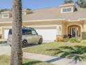Well-maintained beige home with an arched entryway, manicured lawn, and attached two-car garage on a sunny day at 1903 Turnbull Lakes Dr # 1903, New Smyrna Beach, FL 32168