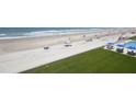 An aerial view of a sandy beach with people relaxing under tents and umbrellas next to a pool and green lawn at 4435 S Atlantic Ave # 416, Port Orange, FL 32127
