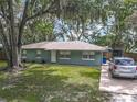 View of a single-story home with a well-maintained lawn, mature trees, and a paved driveway at 1331 Needle Palm Dr, Edgewater, FL 32132