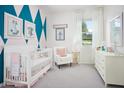 Bedroom with geometric accent wall, crib, armchair, dresser, window with white curtains, and framed animal prints at 1559 Gardiner St, Haines City, FL 33844