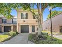 Two-story townhouse showcasing a neutral stucco exterior with a gray garage door and a mature shade tree in the front yard at 2748 Clinton Heights Ct, Oviedo, FL 32765