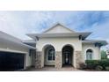 Home's stunning stucco exterior features an arched entryway with stone accents and a three-car garage at 5509 Meadow Hill Loop, Lady Lake, FL 32159