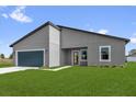 Modern gray home featuring a blue garage door, minimalist landscaping, and a well-maintained green lawn at 4683 Sw 136Th St, Ocala, FL 34473