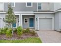 Close-up of a townhome entrance featuring a blue front door, gray garage, and manicured landscaping at 203 River Front Way, Edgewater, FL 32141