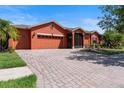 Paver driveway leading to a spacious two-car garage of a one-story home with beautifully landscaped lawn at 1221 Glendora N Rd, Kissimmee, FL 34759