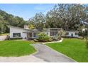 Daytime view of a mid-century modern home featuring professional landscaping, mature trees, and an asphalt driveway at 12550 Lakeshore Dr, Clermont, FL 34711