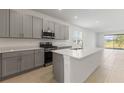 Modern kitchen with gray cabinets, stainless steel appliances, and a large quartz island overlooking the living area at 9097 Wildlight Trl, Wildwood, FL 34785