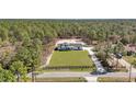 Expansive aerial view of a white farmhouse with black trim surrounded by lush trees and a long driveway at 8827 Sw 137Th Ct, Dunnellon, FL 34432