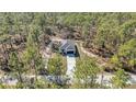 Aerial view of charming single-story home featuring a white exterior, dark garage door, and surrounded by dense forest at 406 Nw Narcissus Rd, Dunnellon, FL 34431