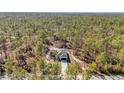 Aerial view of charming single-story home featuring a white exterior, dark garage door, and surrounded by dense forest at 406 Nw Narcissus Rd, Dunnellon, FL 34431