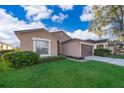 Tan house with brown garage door, lush landscaping, and walkway at 510 Canary Island Cir, Davenport, FL 33837