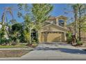 Two story tan house with a large garage surrounded by lush landscaping at 2981 Viscount Cir, Kissimmee, FL 34747