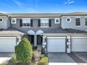 Two-story townhome with gray siding, white garage doors, and landscaping at 10710 Savannah Wood Dr # 107, Orlando, FL 32832