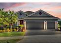 Gray house with three-car garage, palm trees, and landscaped yard at dusk at 943 Gracie Ridge St, Clermont, FL 34715