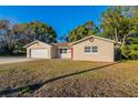 Tan single story house with a red door, attached garage, and well-maintained lawn at 5711 Bolling Dr, Orlando, FL 32808