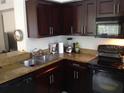 L-shaped kitchen with dark wood cabinets, granite counters and black appliances at 2558 Robert Trent Jones Dr # 1427, Orlando, FL 32835