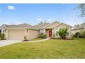 Beige house with red front door, two-car garage, and landscaping at 2984 Cedar Glen Pl, Oviedo, FL 32765