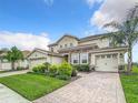 Gorgeous two-story home with a tile roof, landscaping, and a brick-paved driveway leading to a three-car garage at 8886 Fallen Oak Dr, Davenport, FL 33896