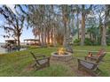 Scenic backyard featuring a stone fire pit and Adirondack chairs in a grassy area with lake and mature trees at 2250 W County Road 44, Eustis, FL 32726