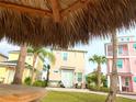 A view from beneath a tiki hut showcases the lush green space and colorful homes of the community at 3020 Latitude Ln, Kissimmee, FL 34747