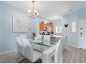 Open-concept dining room with a glass table, white chairs and modern chandelier at 136 Pompano Beach Dr, Kissimmee, FL 34746